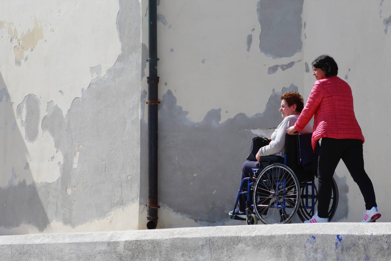 A woman in a wheelchair and another person walking down the sidewalk.